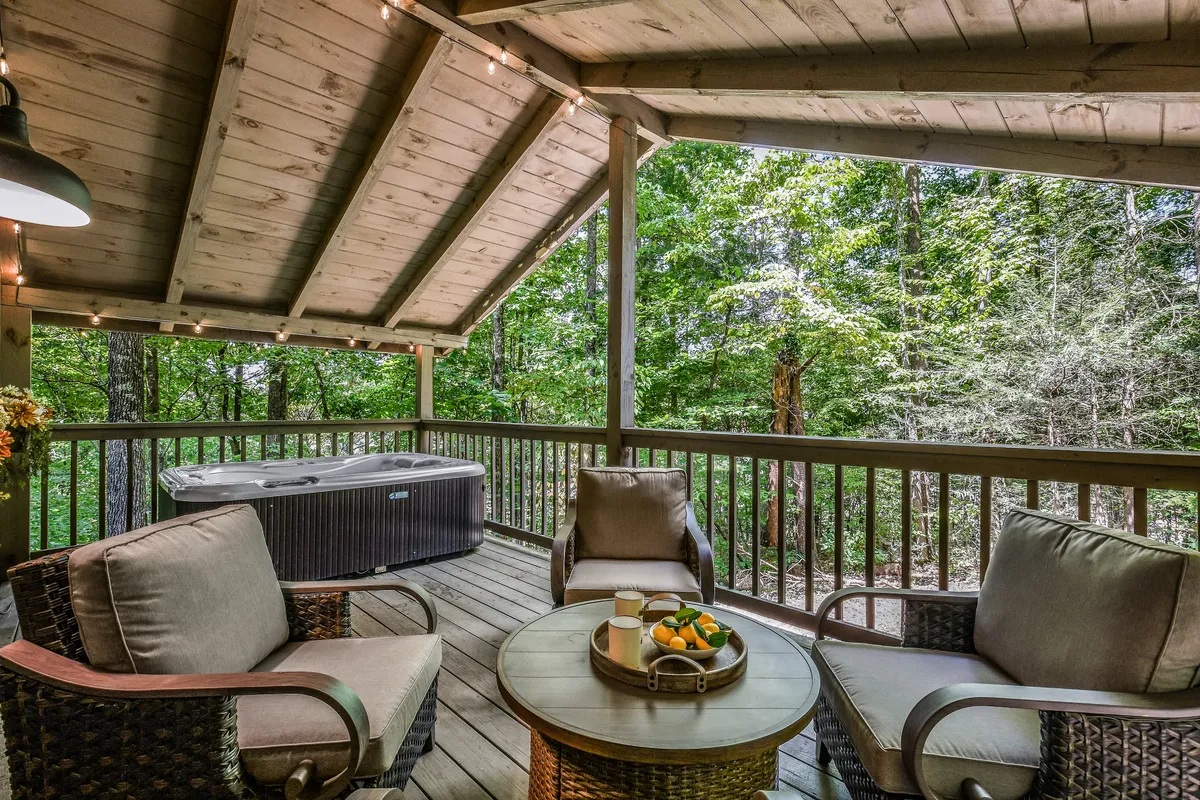 This image features an exterior porch area with a private hot tub, comfortable seating, and a wooden ceiling, all surrounded by lush greenery. The tranquil setting invites relaxation and offers a peaceful connection to nature, with space for both group gatherings and quiet moments.