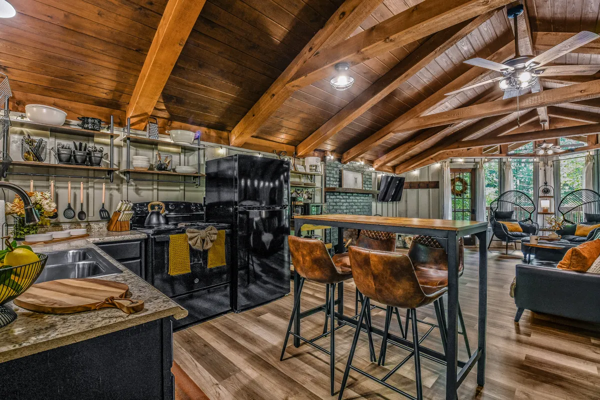 This image showcases the fully equipped kitchen area with a kitchen island, hanging lights, open shelving, and a comfortable seating area with large windows letting in ample natural light. The inviting kitchen, combined with a clear view of the adjacent living space, reinforces the studio's unified flow and readiness for family meals or romantic dinners.