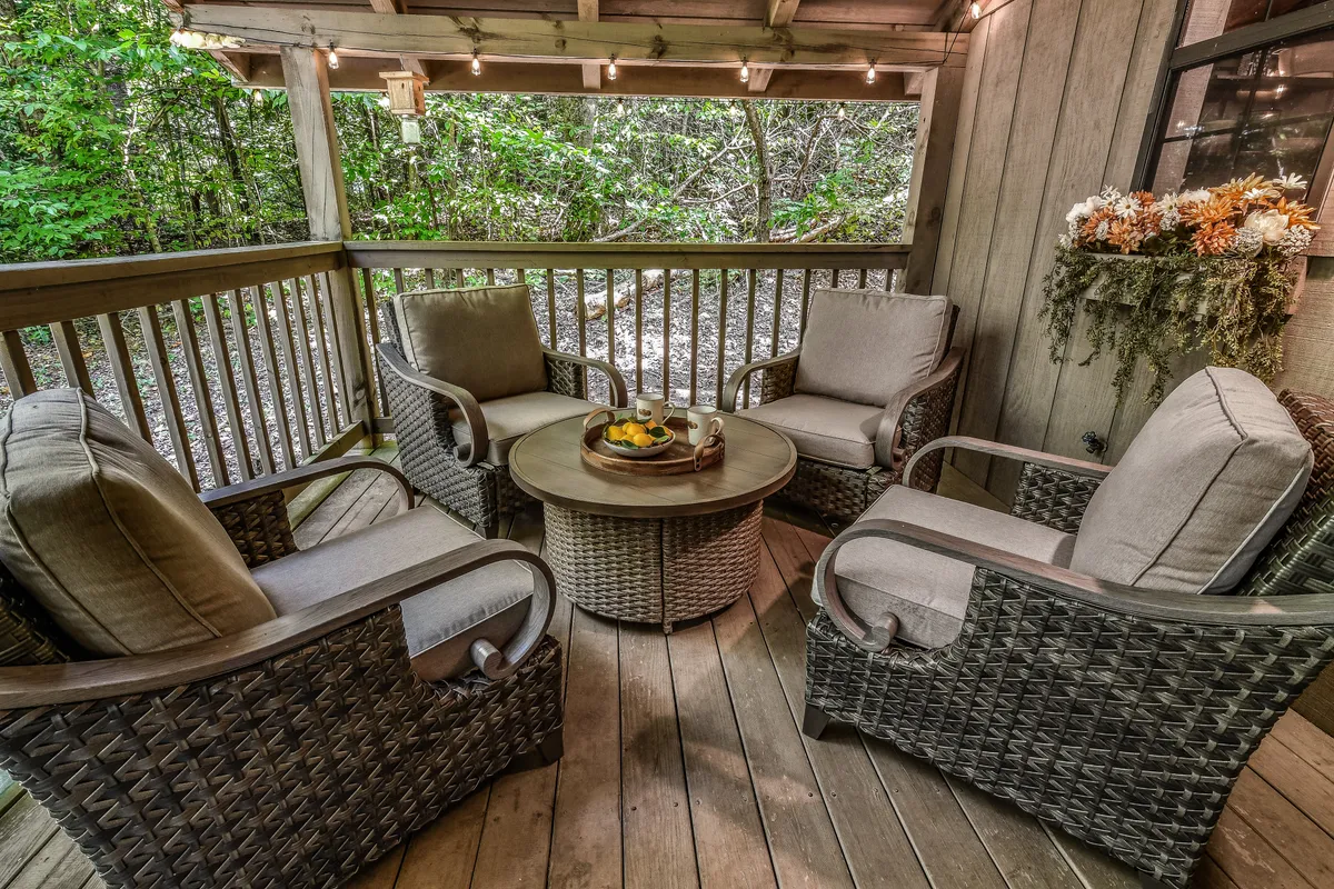 A comfortable outdoor seating area with plush chairs and a decorative table centerpiece, set against a lush, green backdrop. The area is designed for relaxation or conversation, with morning light softly filtering through the trees.